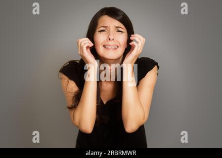 Jeune femme en pleurs éperdus avec elle les mains jointes dans l'angoisse debout avec les yeux baissés contre un fond studio blanc Banque D'Images