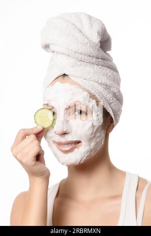 Femme souriante avec ses cheveux attachés dans une serviette blanche et un masque facial nourrissant nettoyant en profondeur appliqué sur sa peau tenant une tranche rafraîchissante de Banque D'Images