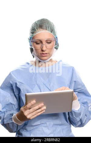 Séduisante femme médecin ou chirurgien dans les gommages et une blouse chirurgicale, lunettes et casquette entrant des informations sur le patient sur un ordinateur tablette, isolé sur Banque D'Images