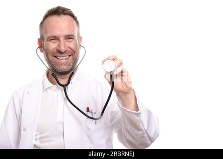 Médecin homme souriant non rasé tenant le disque d'un stéthoscope dans sa main prêt à faire un examen alors qu'il regarde vers le bas la caméra, isolé sur Banque D'Images