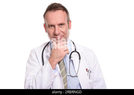 Médecin d'âge moyen réfléchi dans une blouse de laboratoire blanche et stéthoscope regardant la caméra avec sa main contre son menton et un sourire tranquille de Banque D'Images