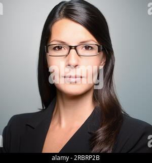 Attrayante jeune femme d'affaires élégante avec une expression attentive regardant directement la caméra, gros plan de son visage sur un fond gris avec Banque D'Images