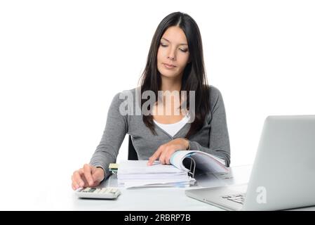 Jeune femme vérifiant un rapport ou des factures dans un grand classeur de bureau faisant des calculs manuels pour vérifier les chiffres sur une calculatrice de bureau Banque D'Images