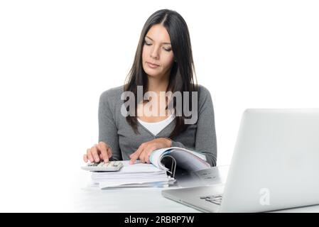 Jeune femme vérifiant un rapport ou des factures dans un grand classeur de bureau faisant des calculs manuels pour vérifier les chiffres sur une calculatrice de bureau Banque D'Images