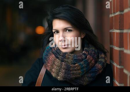 Élégant Pretty Young Woman dans la mode d'automne penché sur le pilier de brique rouge, regardant la caméra Banque D'Images