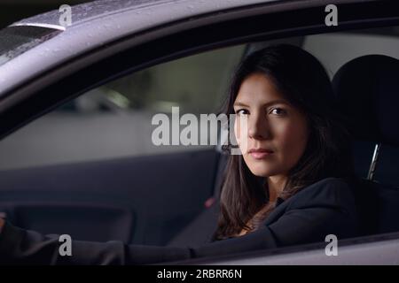 Vue à travers le pare-brise avec des reflets de lumières d'une jeune femme sérieuse conduisant sa voiture la nuit alors qu'elle se rend à la maison après le travail regardant Banque D'Images