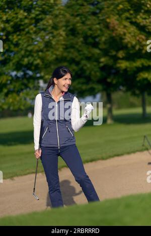 Golfeuse motivée faisant un premier geste de succès et de jubilation après avoir joué son coup pour sortir d'un bunker de sable sur un terrain de golf Banque D'Images