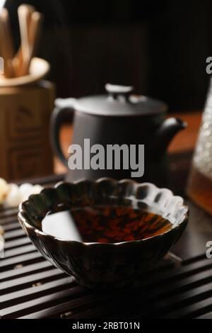 Tasse avec thé pu-erh fraîchement infusé sur plateau en bois, gros plan Banque D'Images