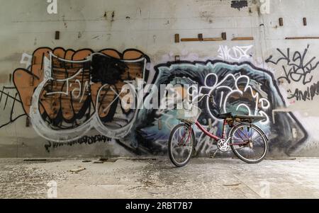 Bangkok, Thaïlande - 08 juillet 2023 - Un vélo rouge est garé à côté des motifs de graffiti sur le mur, dans le bâtiment abandonné. Espace pour le texte Banque D'Images