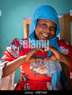 Charmante dame tchadienne, rayonnant brillamment dans son hijab bleu vibrant, forme un signe sincère avec ses mains Banque D'Images