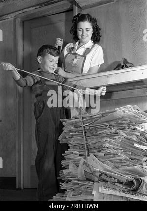 États-Unis : février 1942. Un garçon patriotique qui fait sa part pour l'effort de guerre du front intérieur, attache une corde autour d'une pile de journaux pour recyclage. Banque D'Images