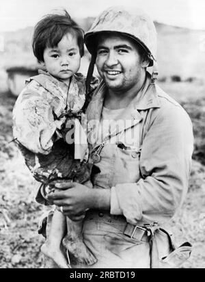 Okinawa, Japon : 21 mai 1945 Un compagnon de pharmacien attaché à la première division des Marines tient une jeune fille autochtone qui a été légèrement blessée lorsque les Marines ont attaqué une base de tireurs d'élite japonais. Banque D'Images