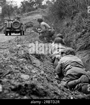 Saint-Lo, France, le 24 juillet 1944 des soldats américains se mettent en avant dans leur trou de renard le long d'une route, alors qu'ils esquivent les tirs de mortier et de mitrailleuses allemands. Banque D'Images