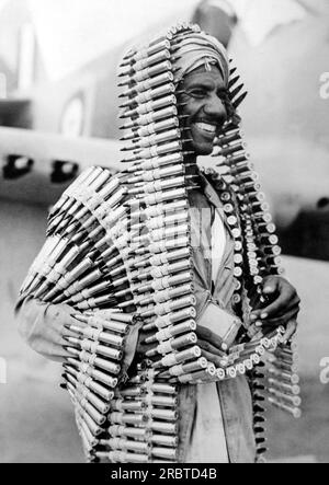 Libye : c. 1941 un assistant arabe d'un armurier de la R.A.F. satisfait de cette tenue originale de munitions pour un avion de chasse "Kittyhawk" contre les convois allemands en Afrique.. Banque D'Images