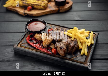 Steak de bœuf striploin avec frites servies à bord sur fond de bois foncé. Viande fraîchement grillée. Dîner sain. Régime méditerranéen. Vue de dessus Banque D'Images