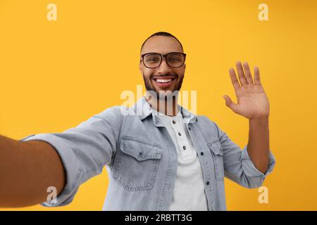 Jeune homme souriant prenant selfie sur fond jaune Banque D'Images