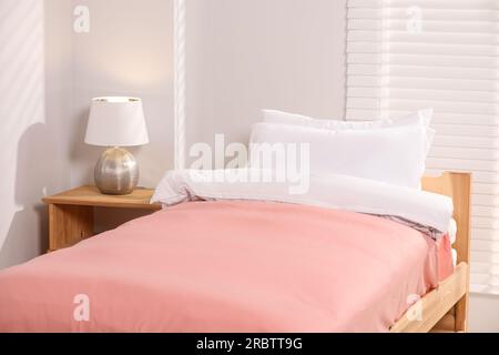 Lit confortable avec coussins et lampe sur table de chevet en bois dans la chambre. Décoration intérieure Banque D'Images