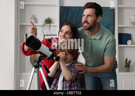 Bonne famille regardant les étoiles à travers le télescope dans la chambre Banque D'Images