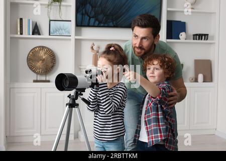 Heureux père et enfants regardant les étoiles à travers le télescope dans la chambre Banque D'Images