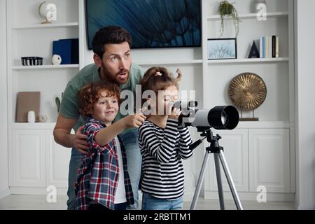 Heureux père et enfants regardant les étoiles à travers le télescope dans la chambre Banque D'Images
