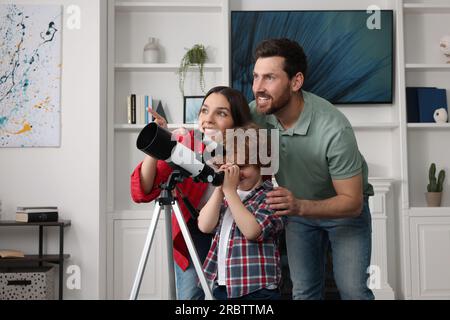 Bonne famille regardant les étoiles à travers le télescope dans la chambre Banque D'Images