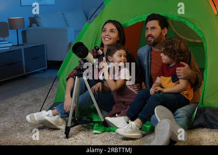 Famille heureuse utilisant le télescope pour regarder les étoiles tout en étant assis dans la tente de camping à l'intérieur Banque D'Images