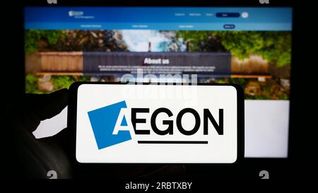 Personne détenant un téléphone portable avec le logo de la société néerlandaise de services financiers Aegon NV sur l'écran devant la page Web de l'entreprise. Concentrez-vous sur l'affichage du téléphone. Banque D'Images