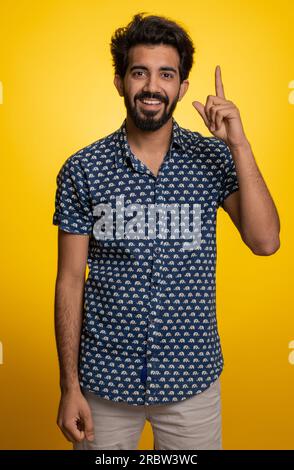 Eureka. Inspiré jeune homme indien pointant du doigt vers le haut avec la bouche ouverte, ayant une bonne idée, plan, démarrage, montrant l'inspiration geste de motivation, solution de problème. Mec hindou barbu sur fond jaune Banque D'Images