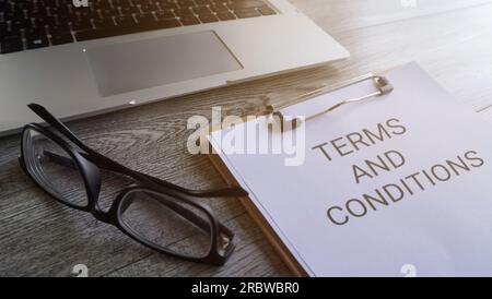 Presse-papiers avec texte TERMES ET CONDITIONS sur la table avec ordinateur portable et lunettes. Banque D'Images