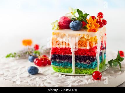 Une tranche de gâteau arc-en-ciel décoré de baies fraîches et de fleurs pour les vacances Banque D'Images