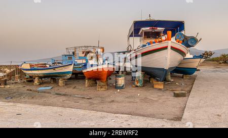 Scène de port de pêche en Grèce avec des bateaux, des palmiers et des scooters au lever du soleil sur une belle journée d'été tranquille Banque D'Images