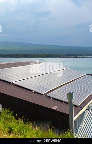 Gros plan de panneaux solaires sur le toit d'une maison sur le fond d'un lac, des montagnes. Photo verticale Banque D'Images