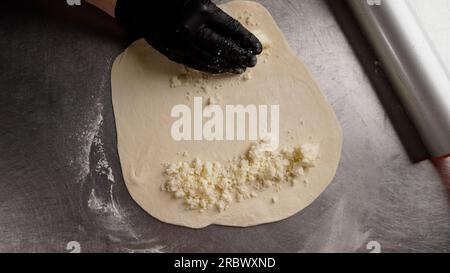 Une femme en gants noirs met la garniture sur la pâte. Procédé de fabrication de produits de boulangerie. Adjarian khachapuri recette - pain au fromage géorgien Banque D'Images