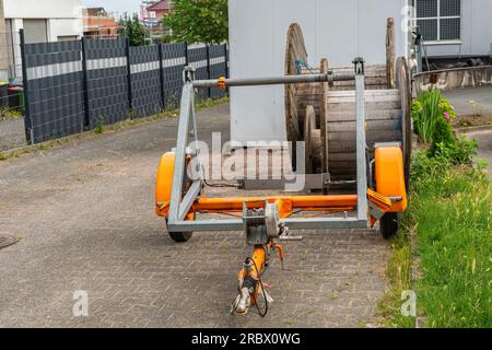 Petite remorque orange pour le transport de bobines de câbles. Bobines en bois vides en arrière-plan. Banque D'Images