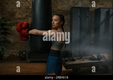 Jeune boxer femme combattant embrassant le sac de frappe après un entraînement intense Banque D'Images