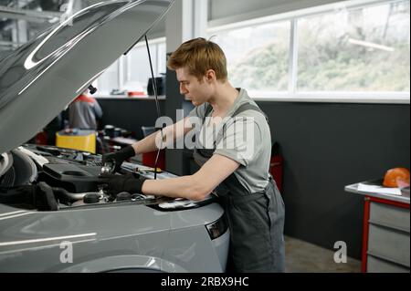 Mécanicien masculin avec clé travaillant sous le capot de voiture ouvert Banque D'Images
