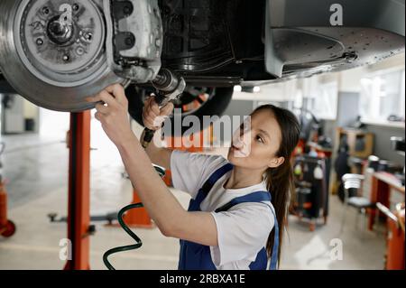 Femme auto mécanicien fixant le train de roulement de la voiture à la station-service Banque D'Images