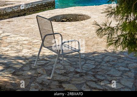 Chaise en métal à l'ombre, côte pavée de pierre de la mer Adriatique, village de Zatoglav, Croatie, Europe Banque D'Images