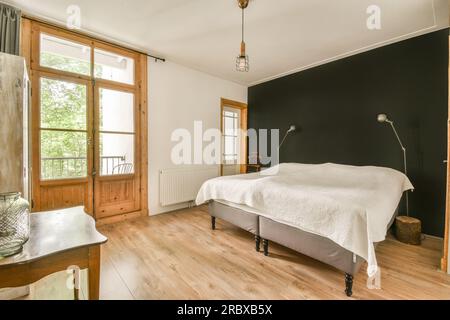 une chambre avec parquet et draps blancs sur le lit, les fenêtres de la chambre sont ouvertes sur l'extérieur Banque D'Images