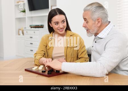 Jouer aux dames. Homme senior apprenant jeune femme à table dans la salle Banque D'Images