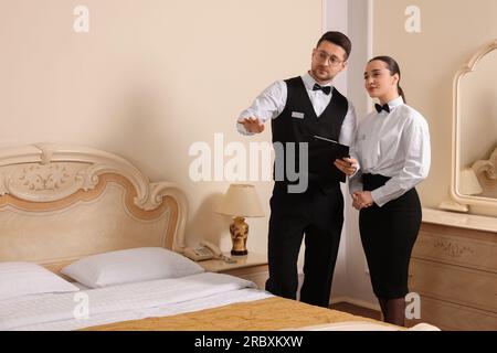 Jeune femme assistant à des cours professionnels de majordome et professeur avec presse-papiers dans la chambre d'hôtel Banque D'Images