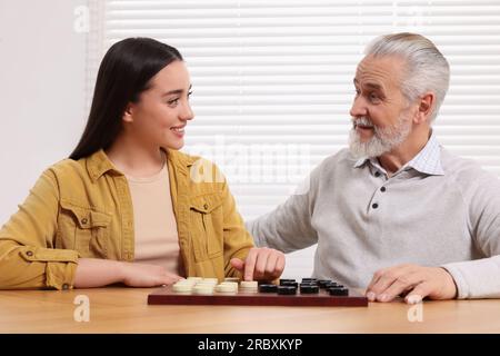Jouer aux dames. Homme senior apprenant jeune femme à table dans la salle Banque D'Images