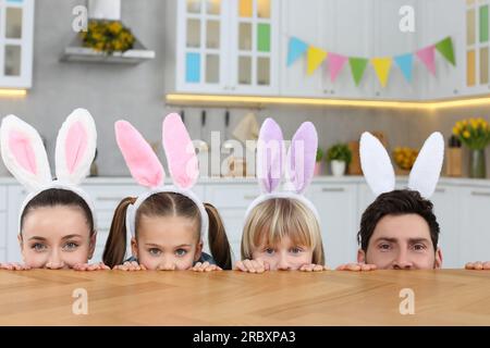 Famille heureuse portant des bandeaux d'oreilles de lapin et jetant un coup d'œil sur la table dans la cuisine. Célébration de Pâques Banque D'Images