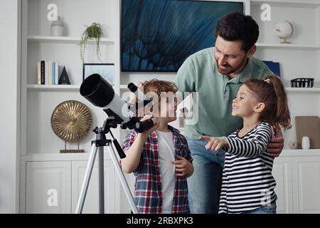 Heureux père et enfants utilisant le télescope pour regarder les étoiles dans la chambre Banque D'Images