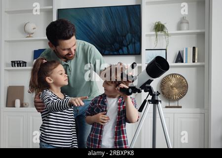 Heureux père et enfants utilisant le télescope pour regarder les étoiles dans la chambre Banque D'Images