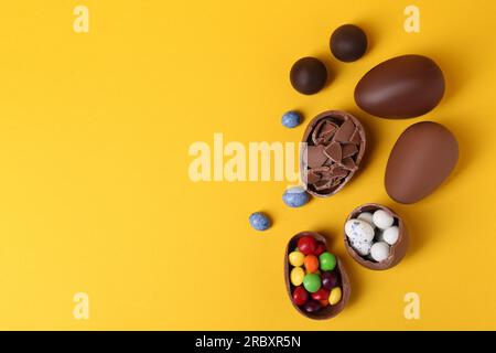 Entiers et les moitiés d'œufs en chocolat avec des bonbons colorés sur fond jaune, ponte plate. Espace pour le texte Banque D'Images