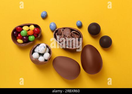 Entiers et les moitiés d'œufs en chocolat avec des bonbons colorés sur fond jaune, ponte plate Banque D'Images