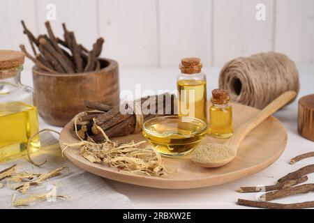 Bâtonnets séchés de racines de réglisse, poudre et huile essentielle sur table en bois blanc Banque D'Images