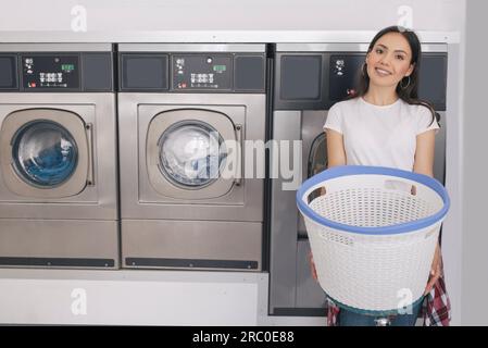 Femme joyeuse Publicité Service de blanchisserie posant près des machines à laver à l'intérieur Banque D'Images