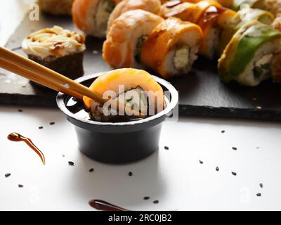 Rouler avec du riz et des crevettes garder les baguettes trempées dans la sauce sur le fond d'un ensemble de rouleaux sur une planche de pierre Banque D'Images